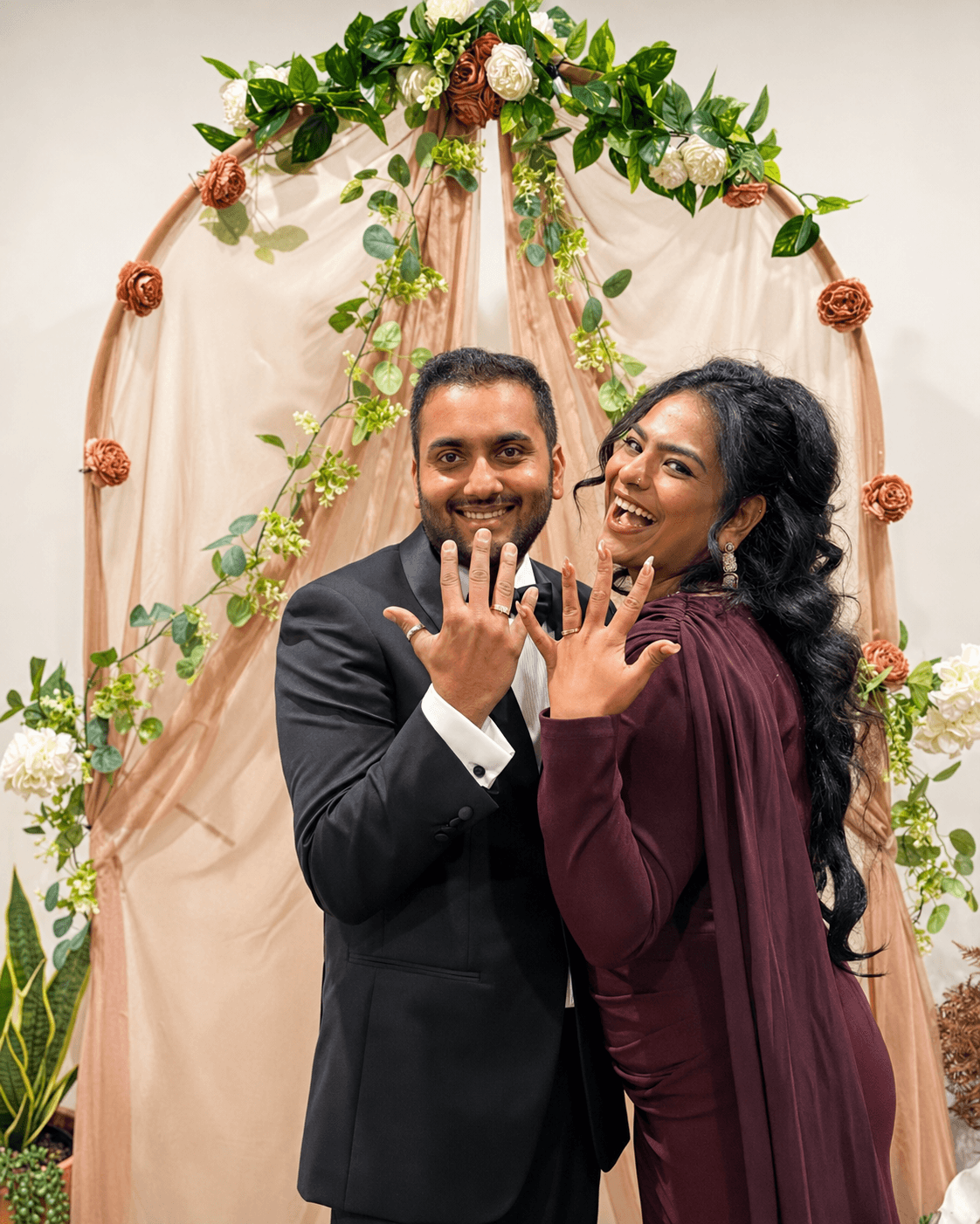 A joyful couple showing their wedding rings under a floral arch at their Melbourne ceremony